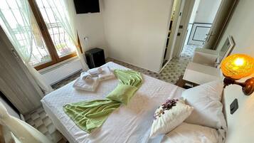 Habitación de hotel con cama, televisor de pantalla plana en la pared, radiador y ventana con cortinas.