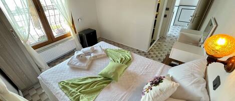 A hotel room with a bed, a flat-screen TV mounted on the wall, a radiator, and a window with curtains.