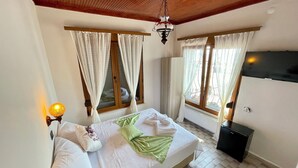 A bedroom with a bed, two windows with curtains, a ceiling fan, a wall-mounted lamp, and a radiator. - Villa Ece Pension (Erdek)
