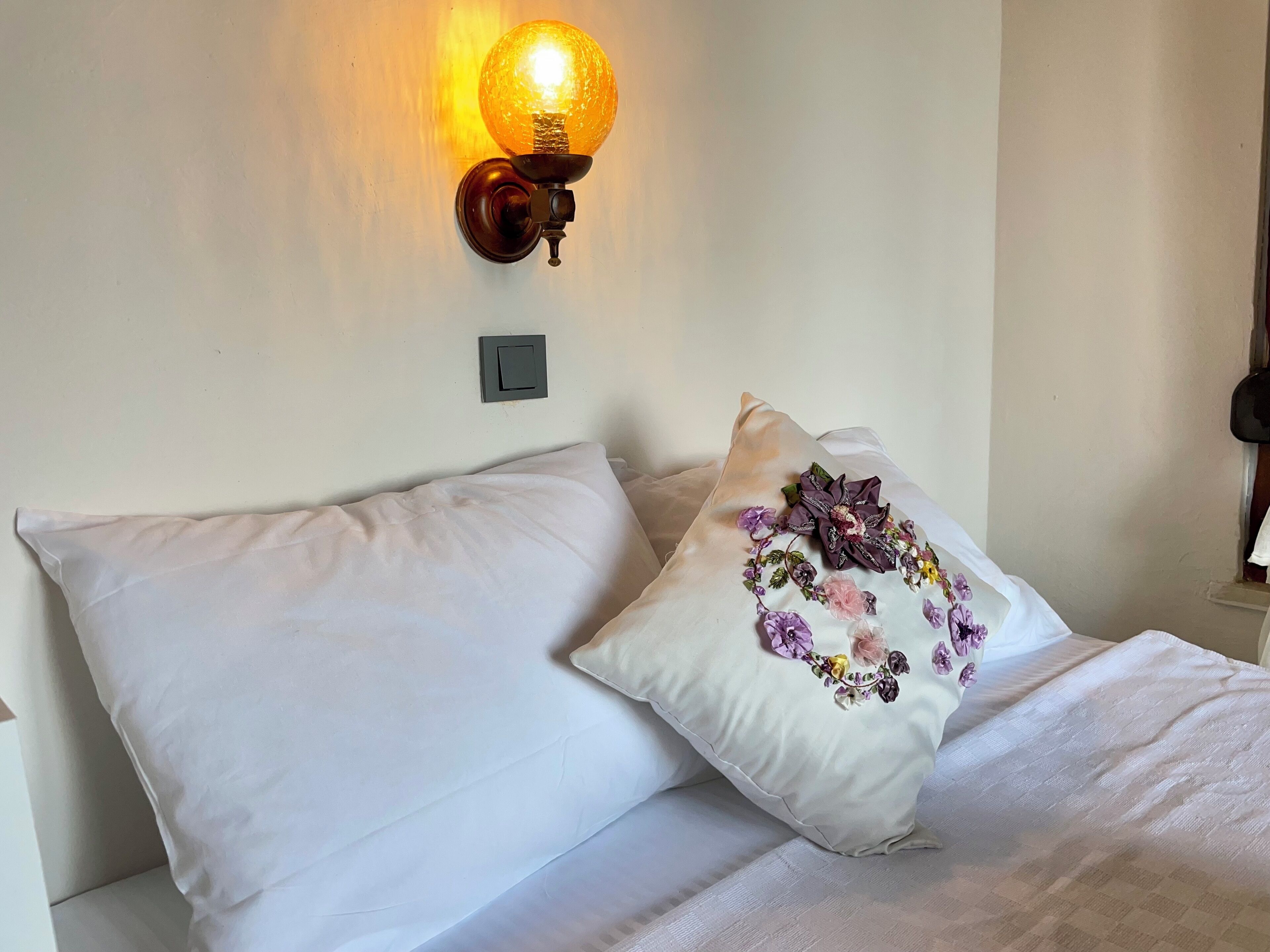 Una cama con ropa blanca y un cojín decorativo con bordado floral.