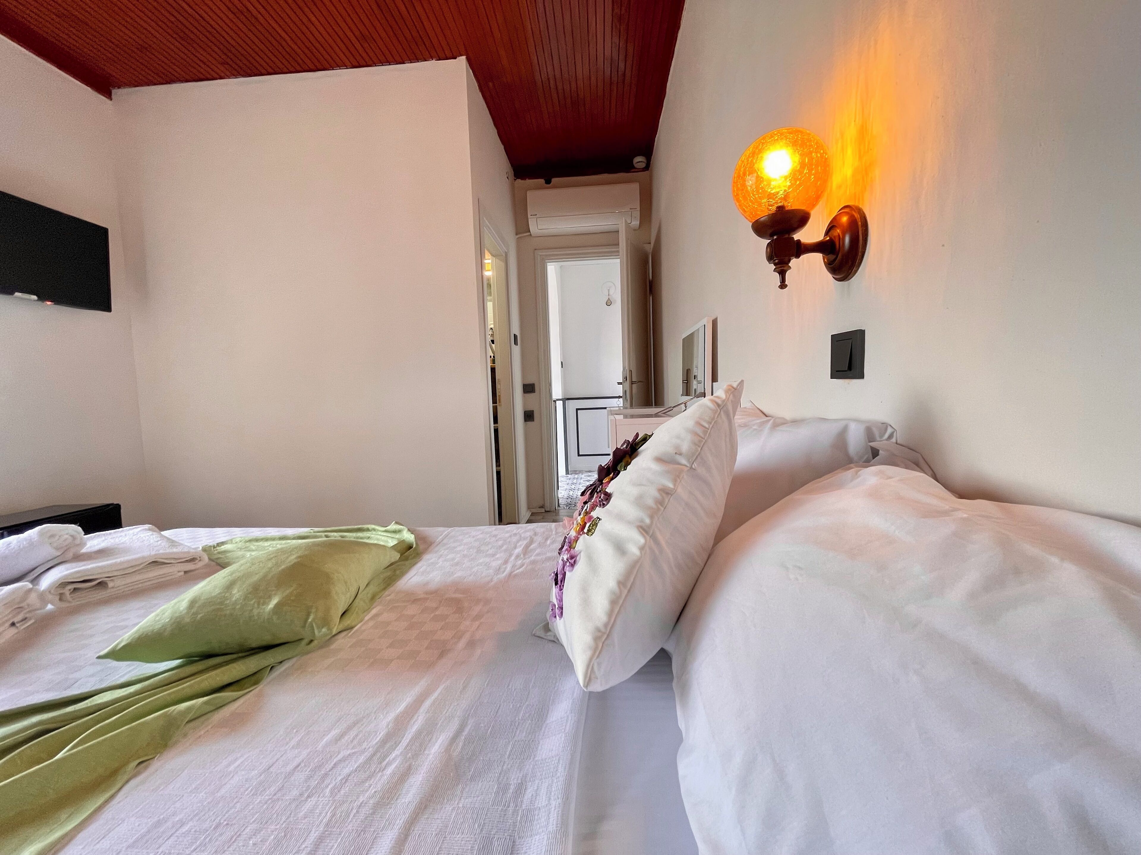 Camera d'albergo con un letto, una coperta verde, cuscini bianchi e una lampada a parete.