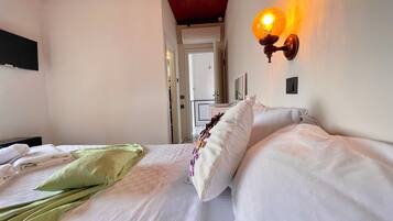 Camera d'albergo con un letto, una coperta verde, cuscini bianchi e una lampada a parete.