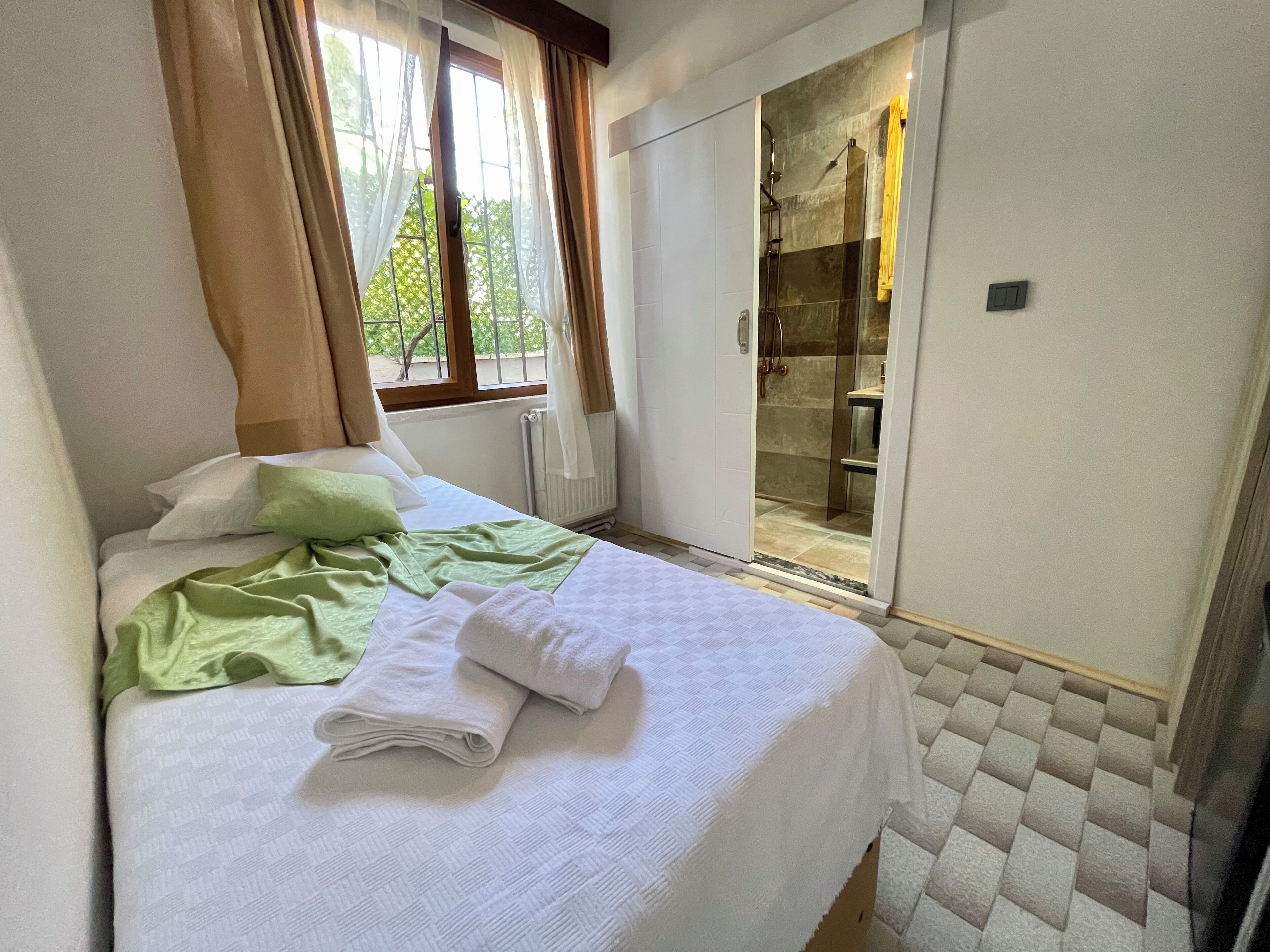 Una habitación de hotel con cama, ventana con cortinas, zona de ducha y un radiador.
