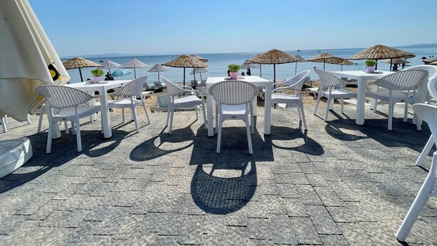 A seaside terrace with white plastic chairs and tables, umbrellas, and a view of the sea. - Villa Ece Pension (Erdek)