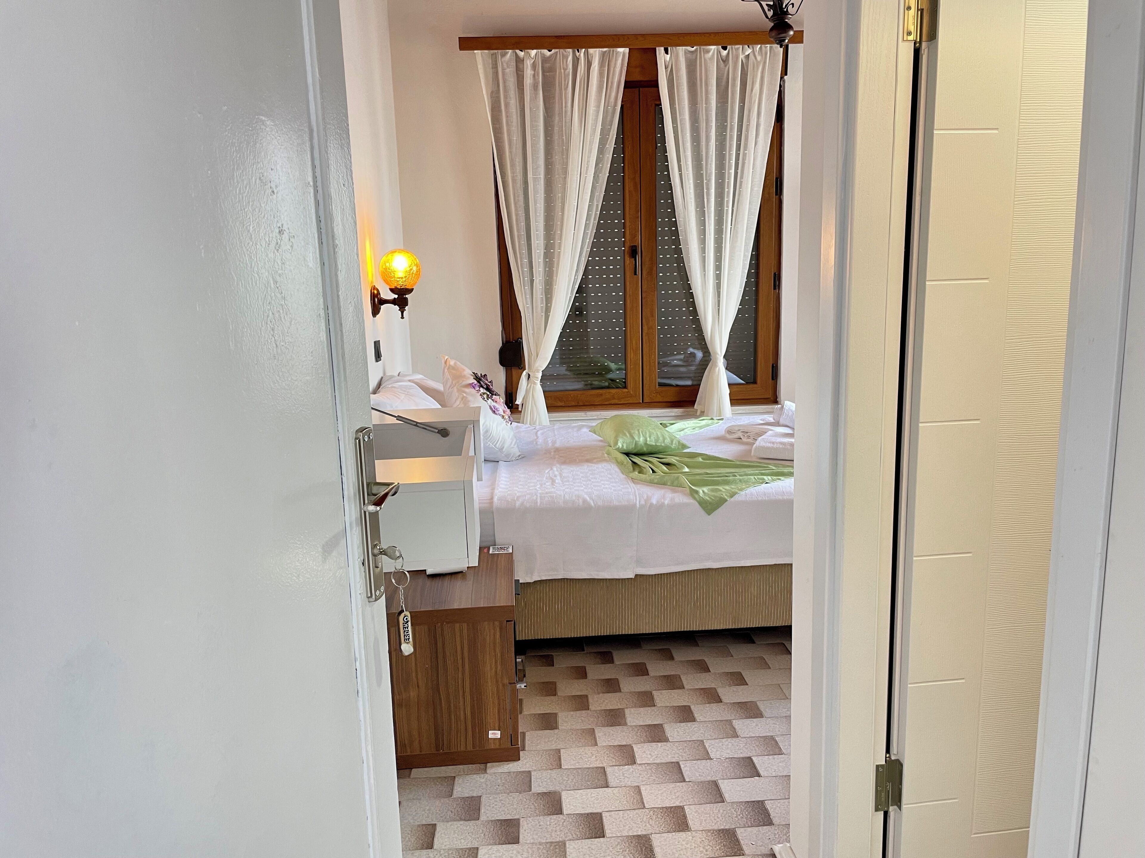 A bedroom with a bed, a nightstand, a lamp, and a window with curtains.