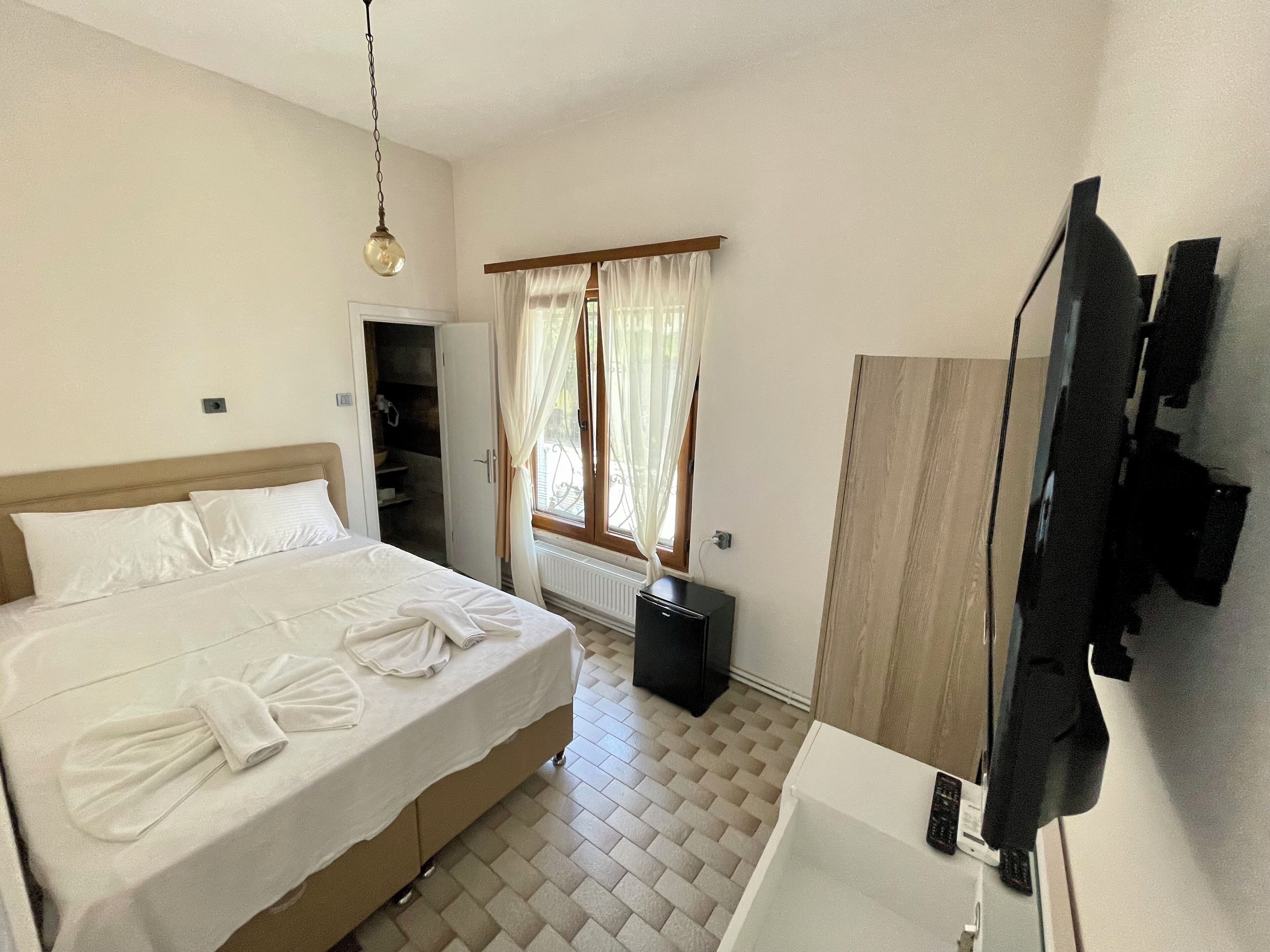 Une chambre d’hôtel comprenant un lit, une armoire, une fenêtre avec des rideaux, un radiateur et un miroir.
