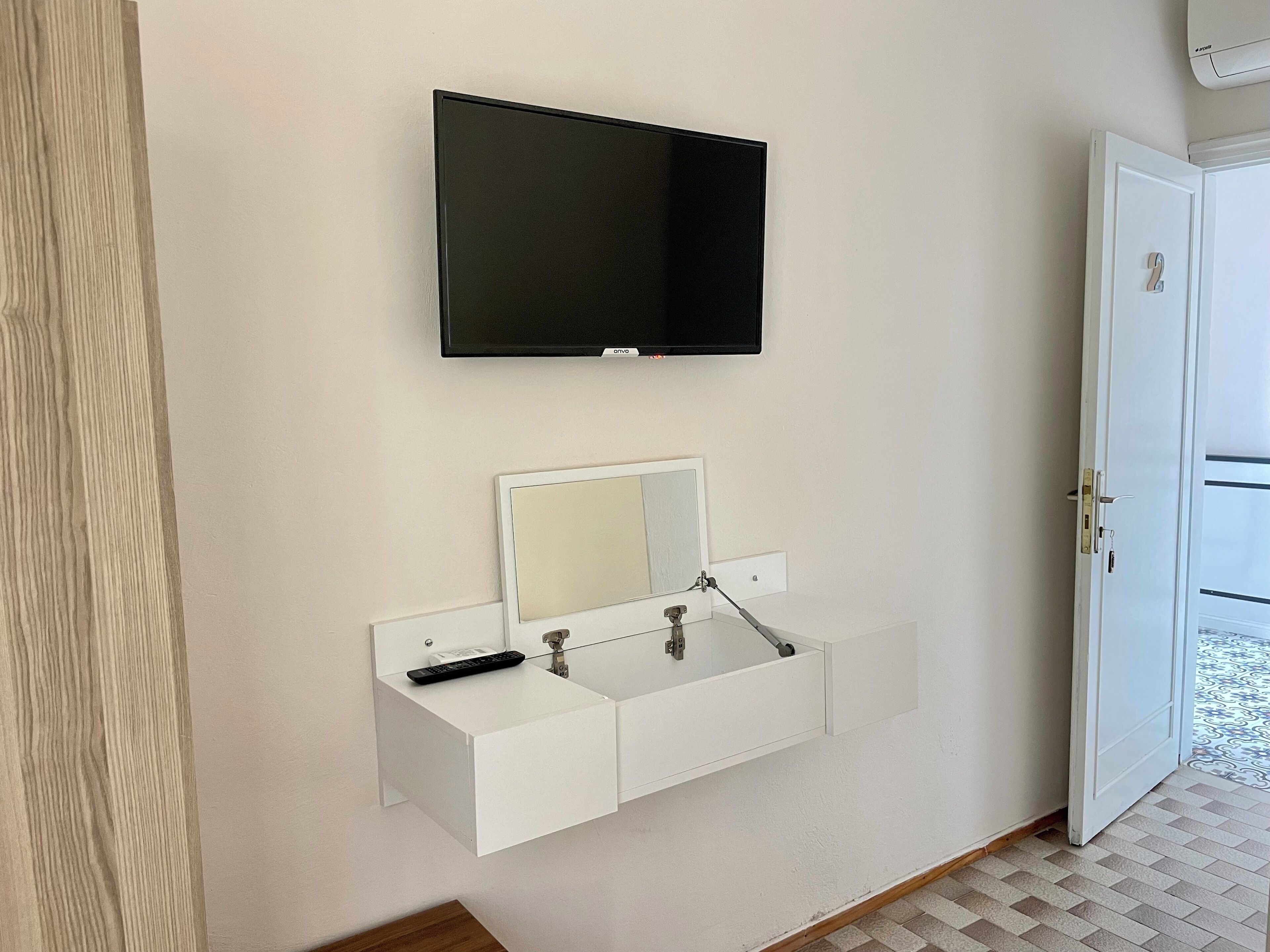 A bathroom with a mounted TV, a sink with a mirror, and a door.