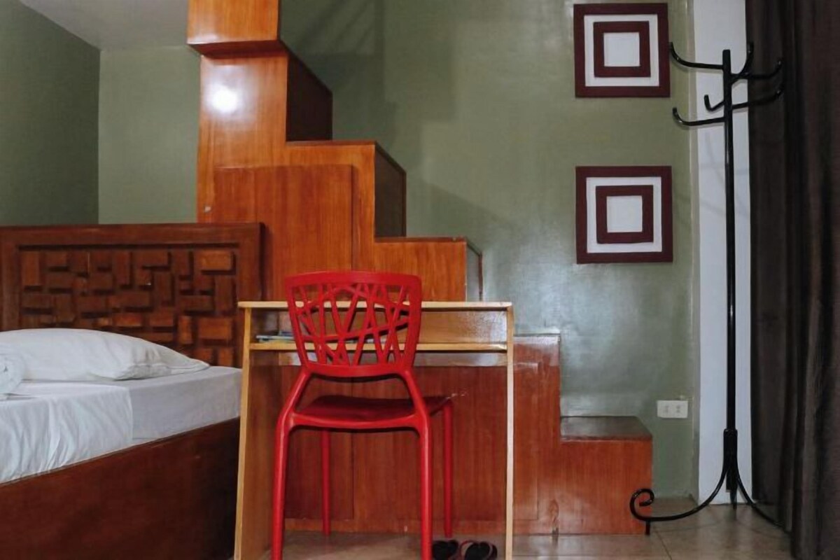 Quarto com cama de madeira, uma cadeira vermelha, escrivaninha e escada.