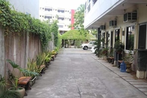 Une ruelle étroite bordée de plantes en pot et où est garée une voiture.