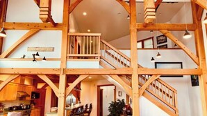 A spacious loft with exposed wooden beams, a central staircase, and a cozy seating area with a sofa and armchairs. - Bay Bluff Haven:  Ocean, Glacier, & Wildlife View (Homer)