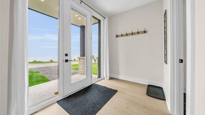 A modern entryway with glass doors leading to a driveway, a black doormat, and a wall-mounted coat rack. - NEW 797 Lakeshore rd Paradise (Selkirk)