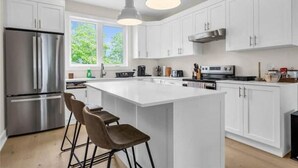 A modern kitchen with white cabinetry, stainless steel appliances, and a central island with bar stools. - NEW 797 Lakeshore rd Paradise (Selkirk)