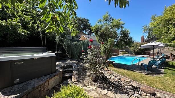 A backyard with a hot tub, a swimming pool, and outdoor seating. - Bring everyone together while enjoying the privacy of three separate living spaces. This unique Medford retreat features a spacious main home, two private guest homes, a seasonal pool, hot tub, fully equipped kitchens, and room for the whole family. (Medford)