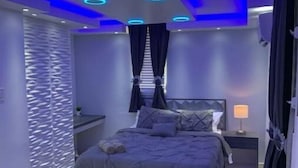 Une chambre à coucher moderne avec un lit, des tables de chevet et une étagère fixée au mur.