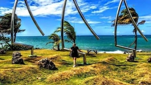 Une plage avec trois sculptures métalliques, une personne debout et une vue sur l’océan.