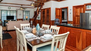 A dining area with a wooden table set for six, white chairs, and a kitchen with wooden cabinets and a stainless steel refrigerator. - Two Bedroom Sea View- Villas De Isla Bonita – Dolphin Dreams Penthouse (San Pedro Town)