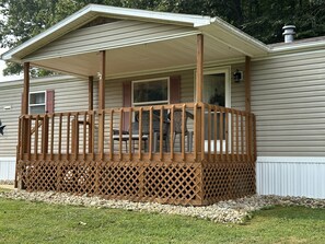 A covered porch with a wooden railing and lattice design, leading to a door. - 1st Choice Lodging- Burr Oak Bungalow (Nelsonville)