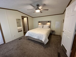 Un dormitorio con una cama individual, ventilador de techo, una puerta y un taburete pequeño.