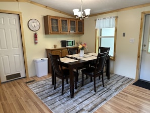 A dining area with a wooden table, four chairs, a vase with flowers, a clock, and wooden cabinets. - 1st Choice Lodging- Burr Oak Bungalow (Nelsonville)