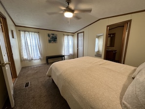 A bedroom with a bed, a ceiling fan, a bench, and a door leading to another room. - 1st Choice Lodging- Burr Oak Bungalow (Nelsonville)