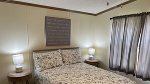 Ein Schlafzimmer mit einem Bett, zwei Nachttischen mit Lampen, einer Wand mit einem motivierenden Zitat und einem Fenster mit Vorhängen.