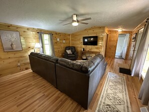 Ein Holzblockhaus-Interieur mit Ledersofa, Fernseher und Deckenventilator.