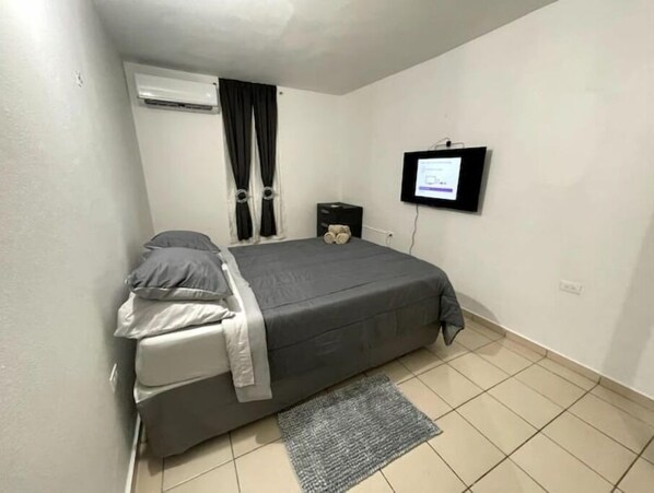 A small, clean room with a bed, a TV, and a window with curtains. - Rincón frente al lago Levittown (Toa Baja Levittown)