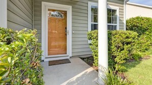 A house with a wooden front door, a porch, and a small garden with bushes. - The Mulberry: huge yard full kitchen 32 minutes to the beach (North Charleston)