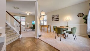 A spacious living room with a staircase, a dining area with green chairs, and a dartboard on the wall. - The Mulberry: huge yard full kitchen 32 minutes to the beach (North Charleston)