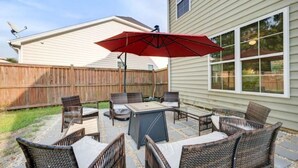 An outdoor patio with a table and chairs, a red umbrella, and a wooden fence. - The Mulberry: huge yard full kitchen 32 minutes to the beach (North Charleston)