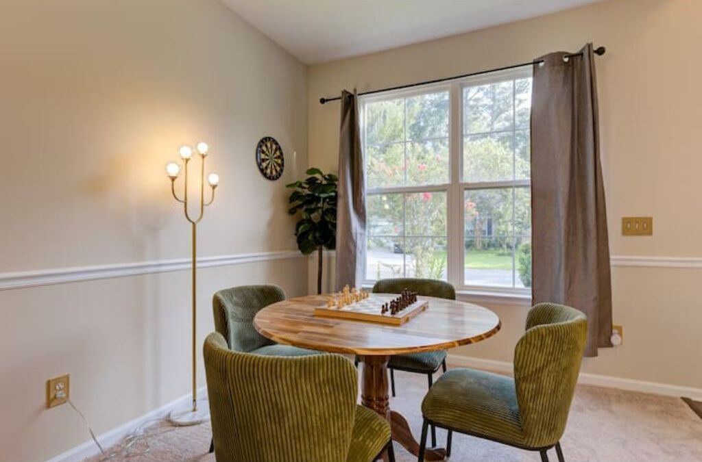 Un coin repas comprenant une table ronde en bois, quatre chaises rembourrées, un lampadaire et une fenêtre avec des rideaux.
