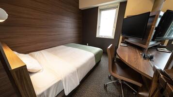 A hotel room with a single bed, a desk with a chair, a television, and a window.
