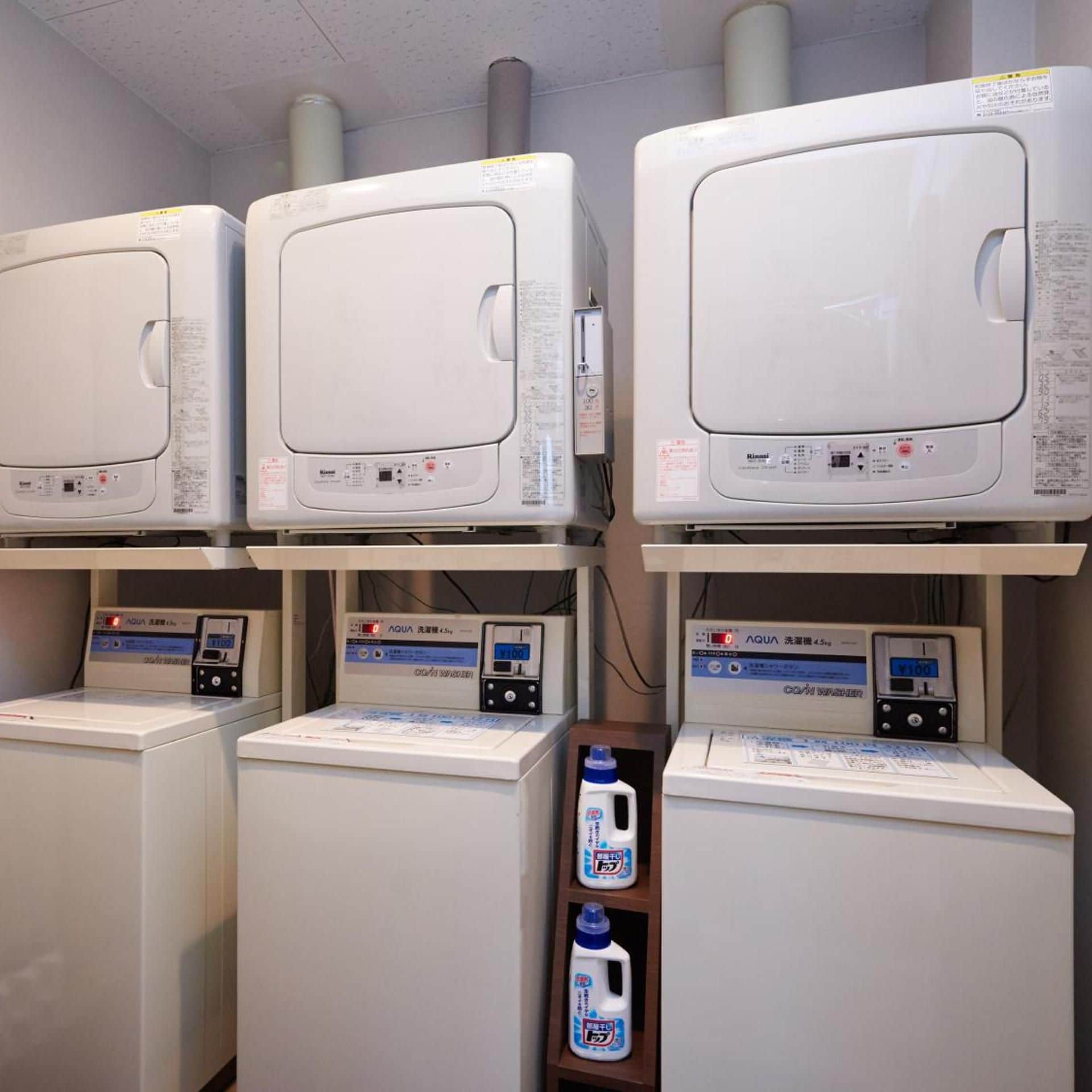 A laundry facility with multiple washing machines and dryers, each with control panels and digital displays.
