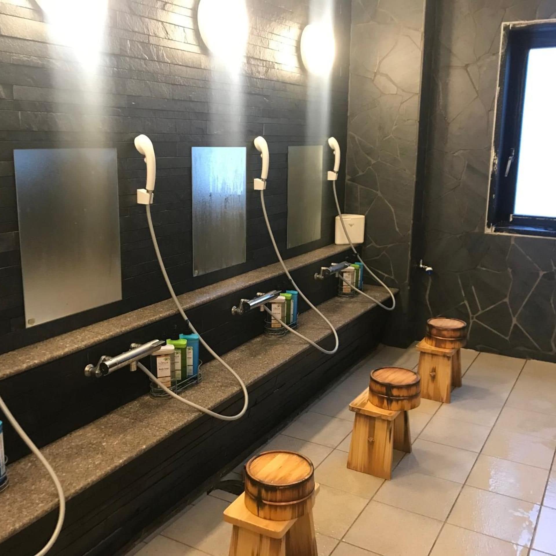 A public restroom with multiple sinks, hand dryers, and a window.