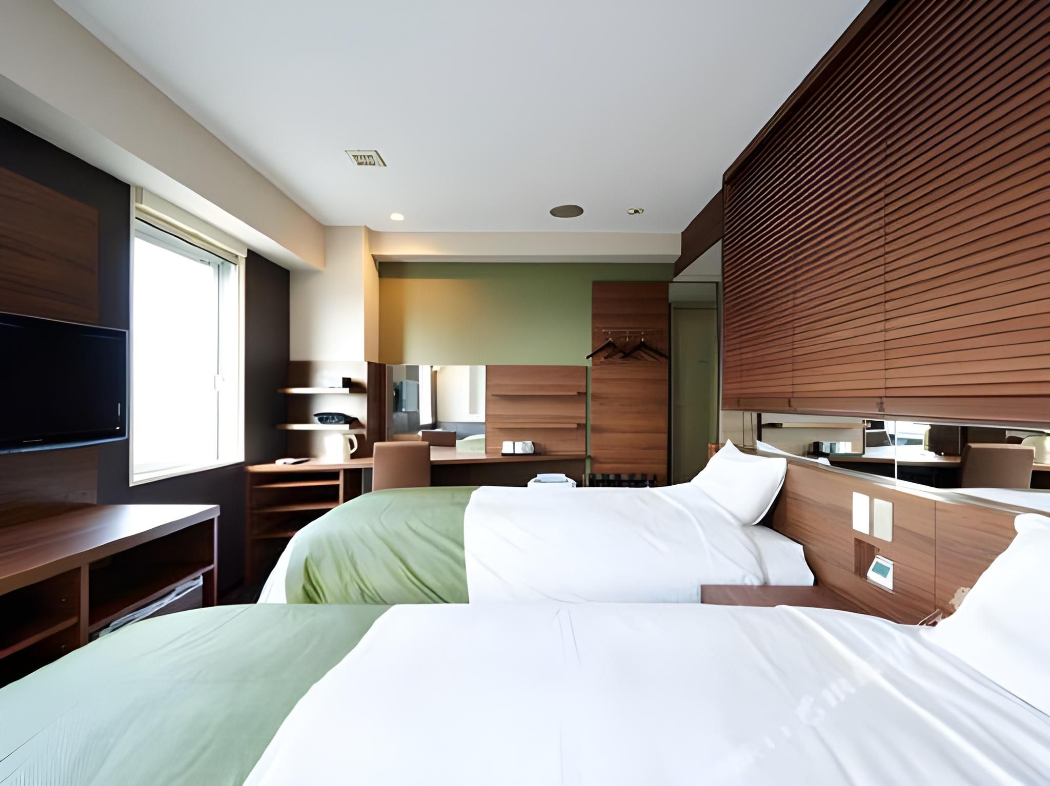 A hotel room with two beds, a TV, a desk, and a bathroom.