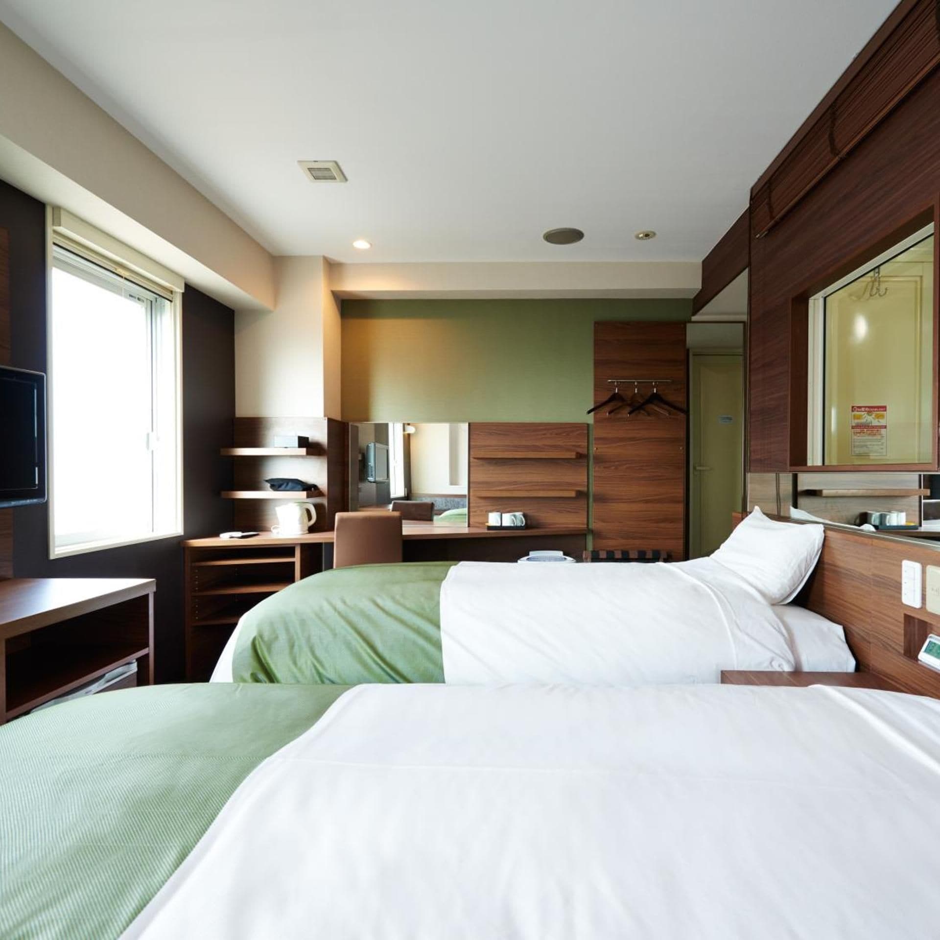 A hotel room with two beds, a desk, a chair, a television, and a mirror.