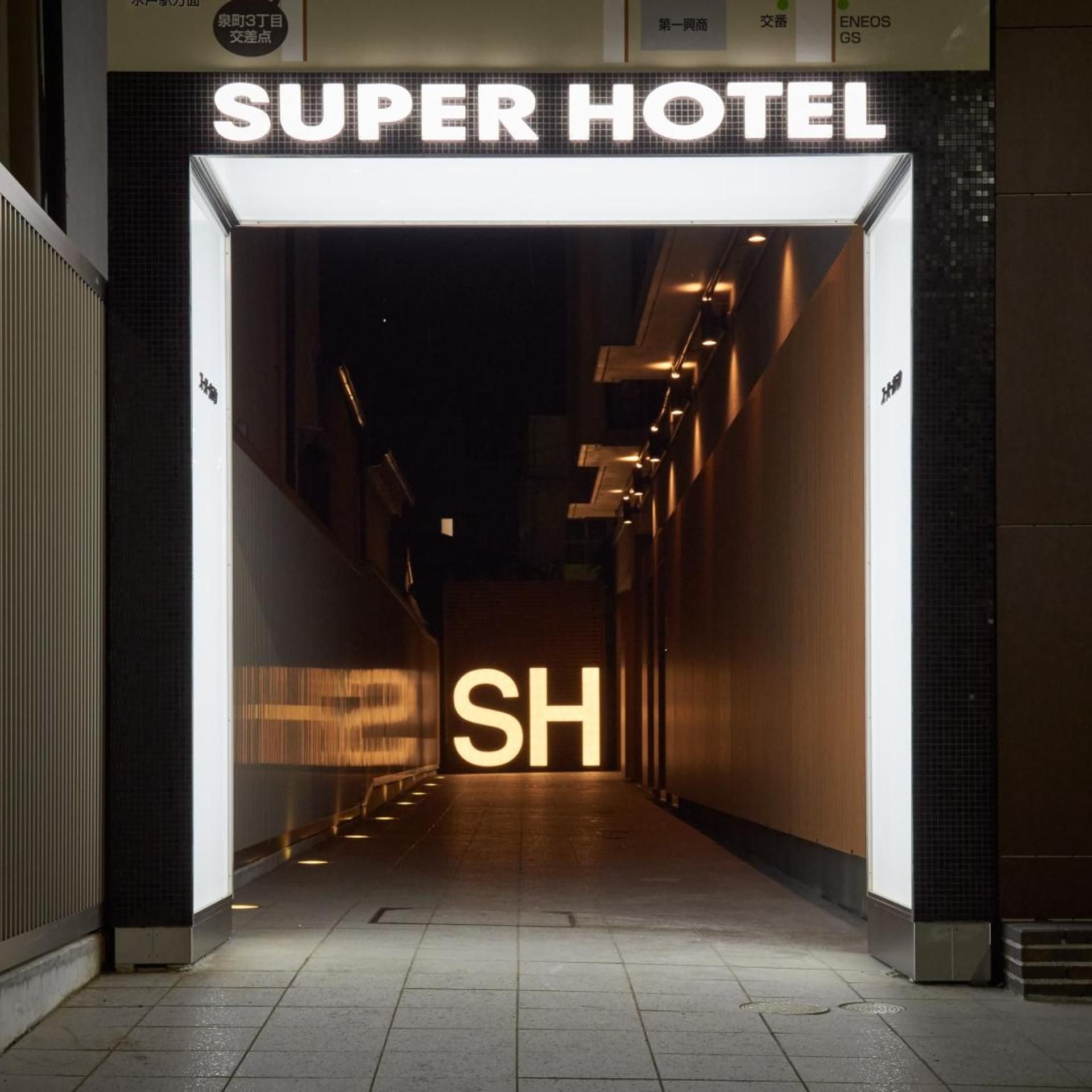 The entrance to a hotel with a prominent 'SUPER HOTEL' sign and a large illuminated 'SH' sign.