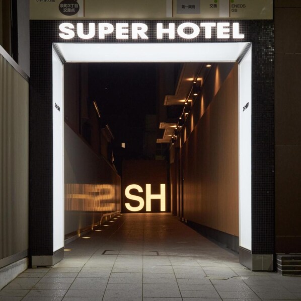 The entrance to a hotel with a prominent 'SUPER HOTEL' sign and a large illuminated 'SH' sign. - Super Hotel Mito Natural Onsen (Mito)
