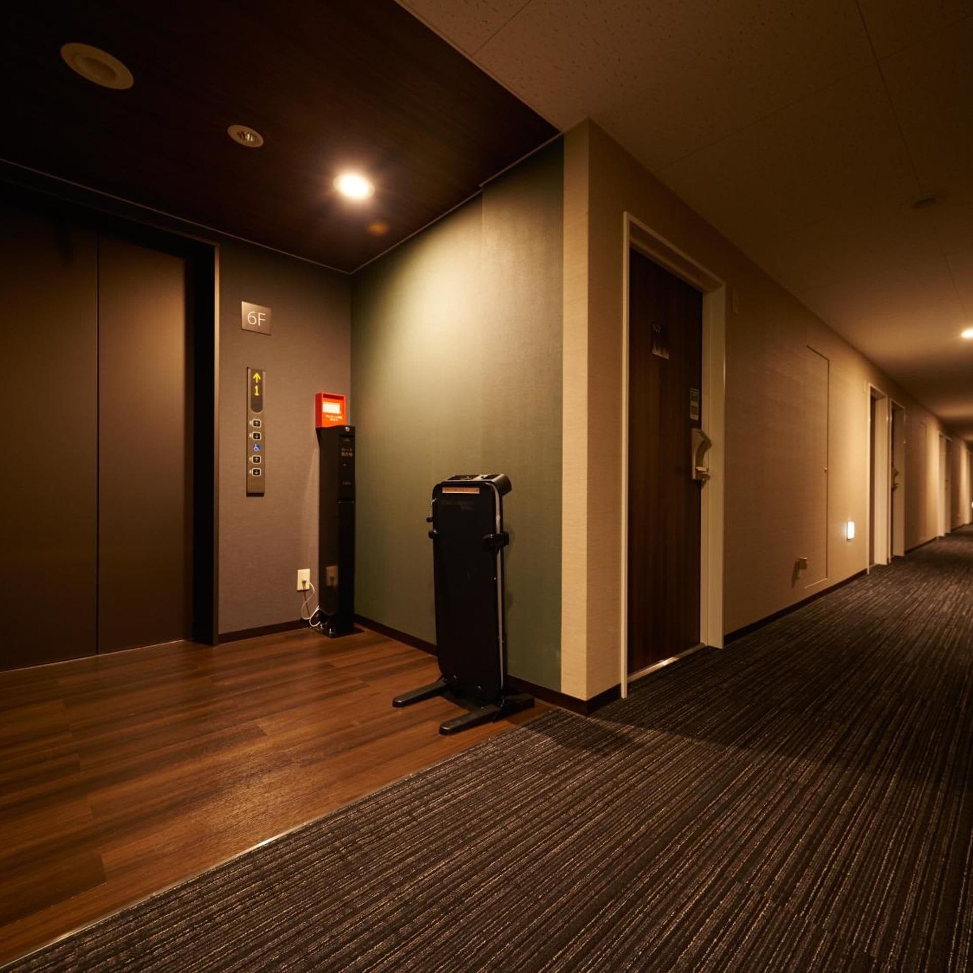 A hotel corridor with a carpeted floor, a trash bin, and doors leading to rooms.