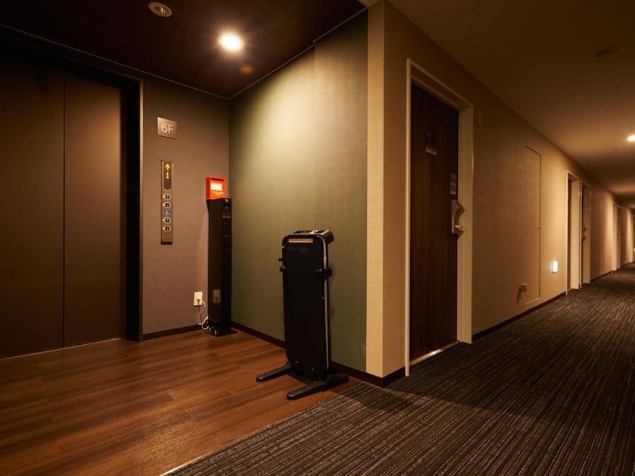 Un couloir d’hôtel avec un sol recouvert de moquette, une poubelle et des portes donnant accès aux chambres.