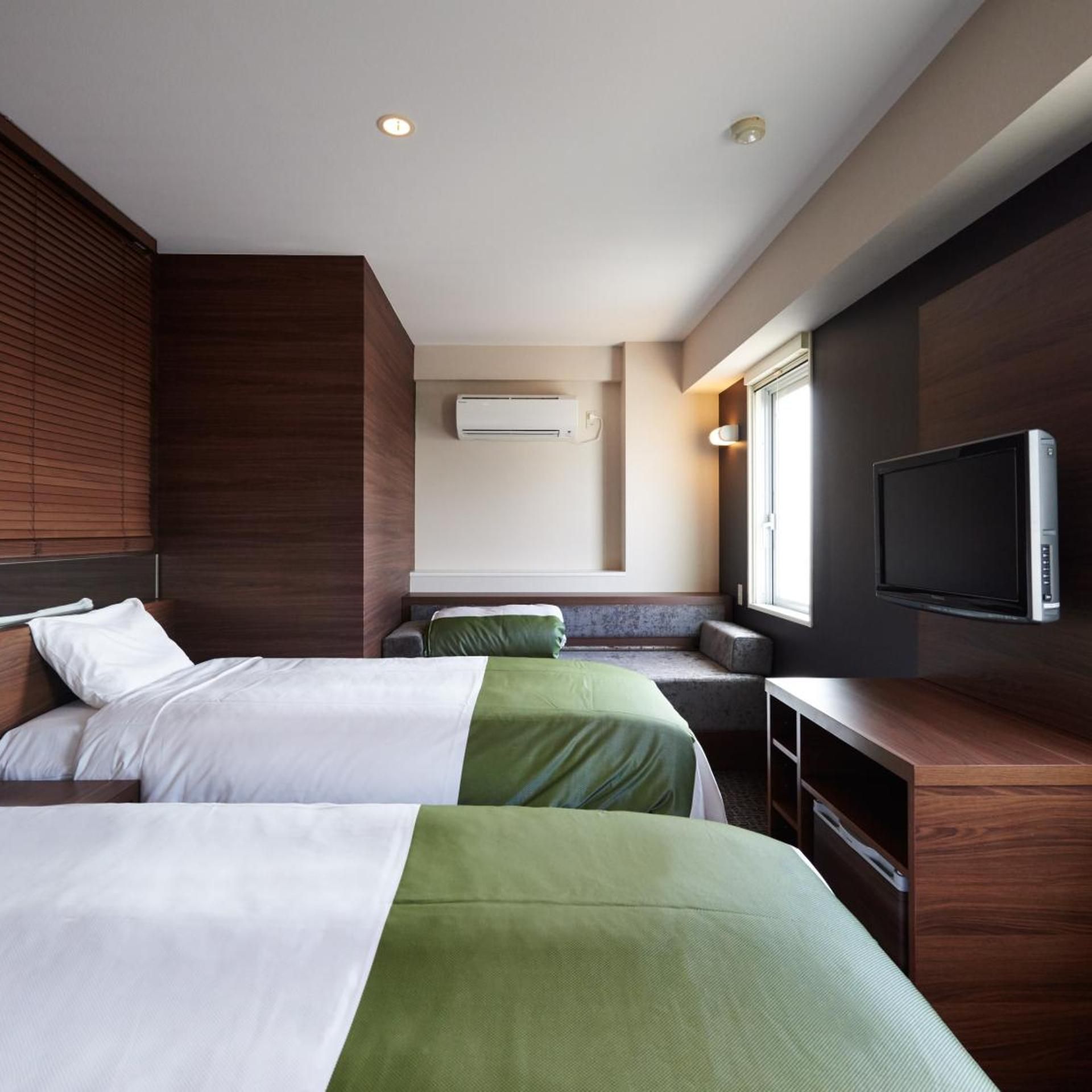 A hotel room with two beds, a TV, an air conditioning unit, and a window.