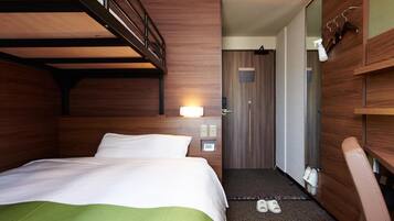 A hotel room with a bunk bed, a desk, a chair, a shoe rack, and a door leading to a bathroom.