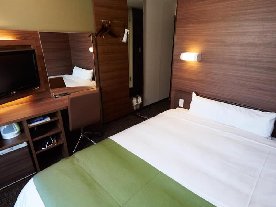 Et hotelværelse med seng, skrivebord, fjernsyn og garderobeskab.
