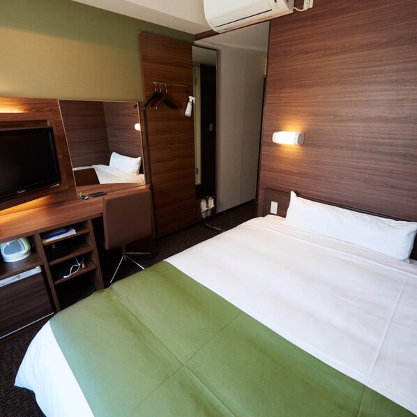 Una habitación de hotel con cama, escritorio, televisor y armario.