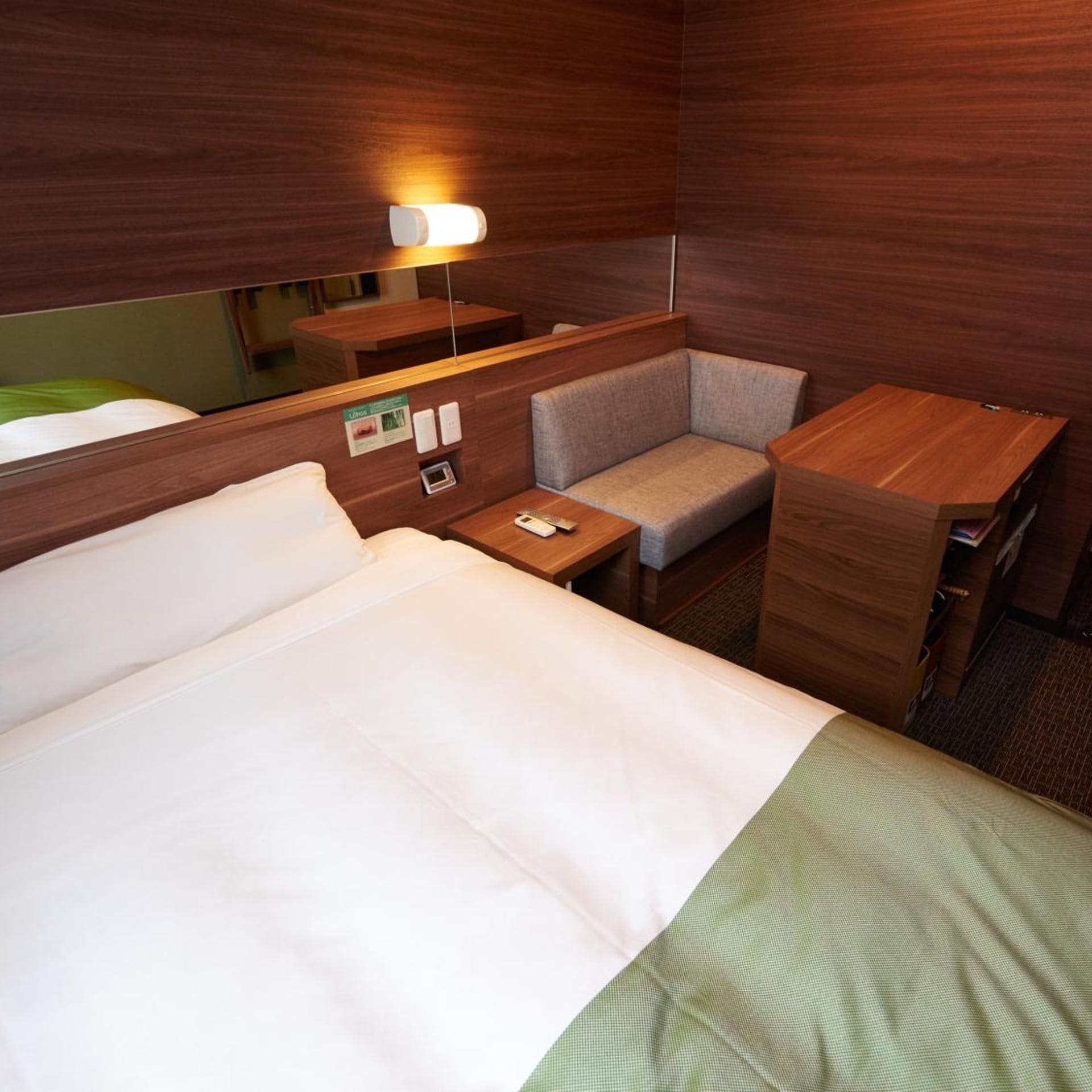 A hotel room with a bed, a small desk, a chair, and a bedside table.