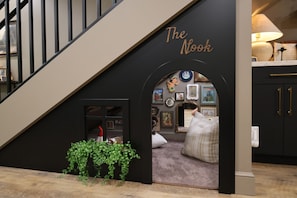 A staircase with a black archway labeled 'The Nook,' leading to a cozy reading area with a sofa and bookshelves.