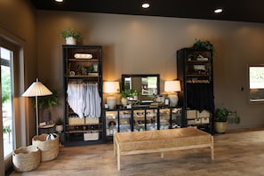 A room with a wooden bench, two black shelving units with various items, a lamp, and a mirror.