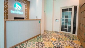 A reception area with a neon sign, patterned floor tiles, a wooden reception desk, and a glass door leading outside. - Bobobox Pods Kota Lama Semarang (Semarang)