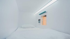 A minimalist room with a single bed, a small window, and a wall-mounted control panel. - Bobobox Pods Kota Lama Semarang (Semarang)
