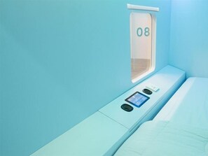 A single-bed room with a window, a control panel, and a number '08' on the window.
